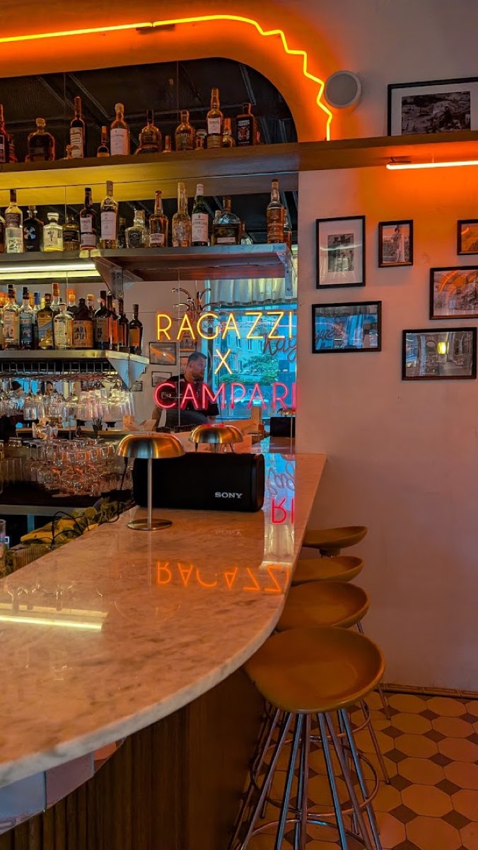 Marmurowy bar Ragazzi z neonowym napisem na lustrze i złotymi stołkami