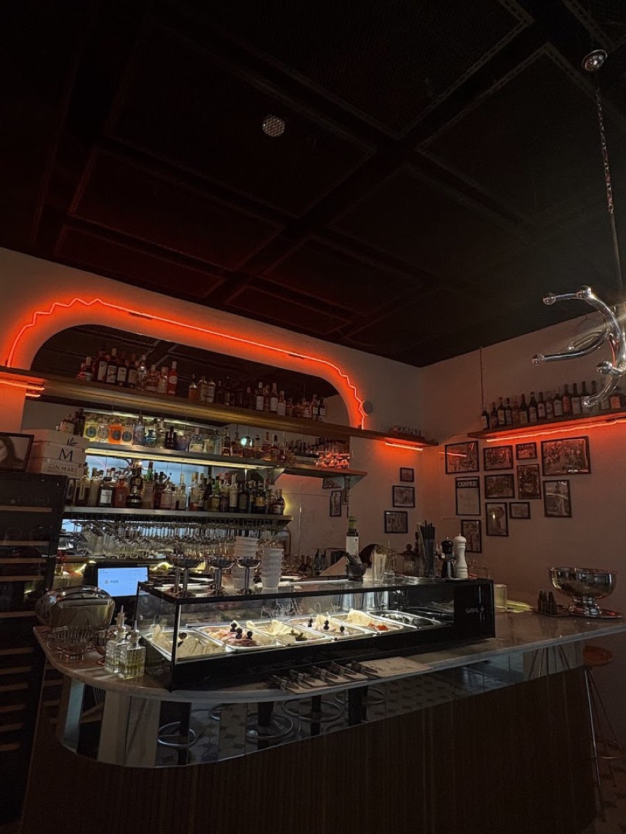 Wnętrze baru: neonowa wstęga nad półką z butelkami i lada z cicchetti